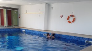 En indendørs swimmingpool med fliserede vægge og en redningskranse på væggen.