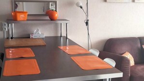 Et moderne spiseområde med et langt bord, orange servietter og en barstol.