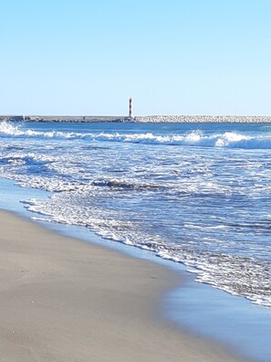 Ein Strand mit Wellen, einem Leuchtturm und einem steinernen Wellenbrecher im Hintergrund.