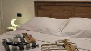 Un lit bien fait, avec du linge de lit blanc, une tête de lit en bois et une table de chevet sur laquelle se trouve une petite lampe de chevet en forme de croissant de lune.