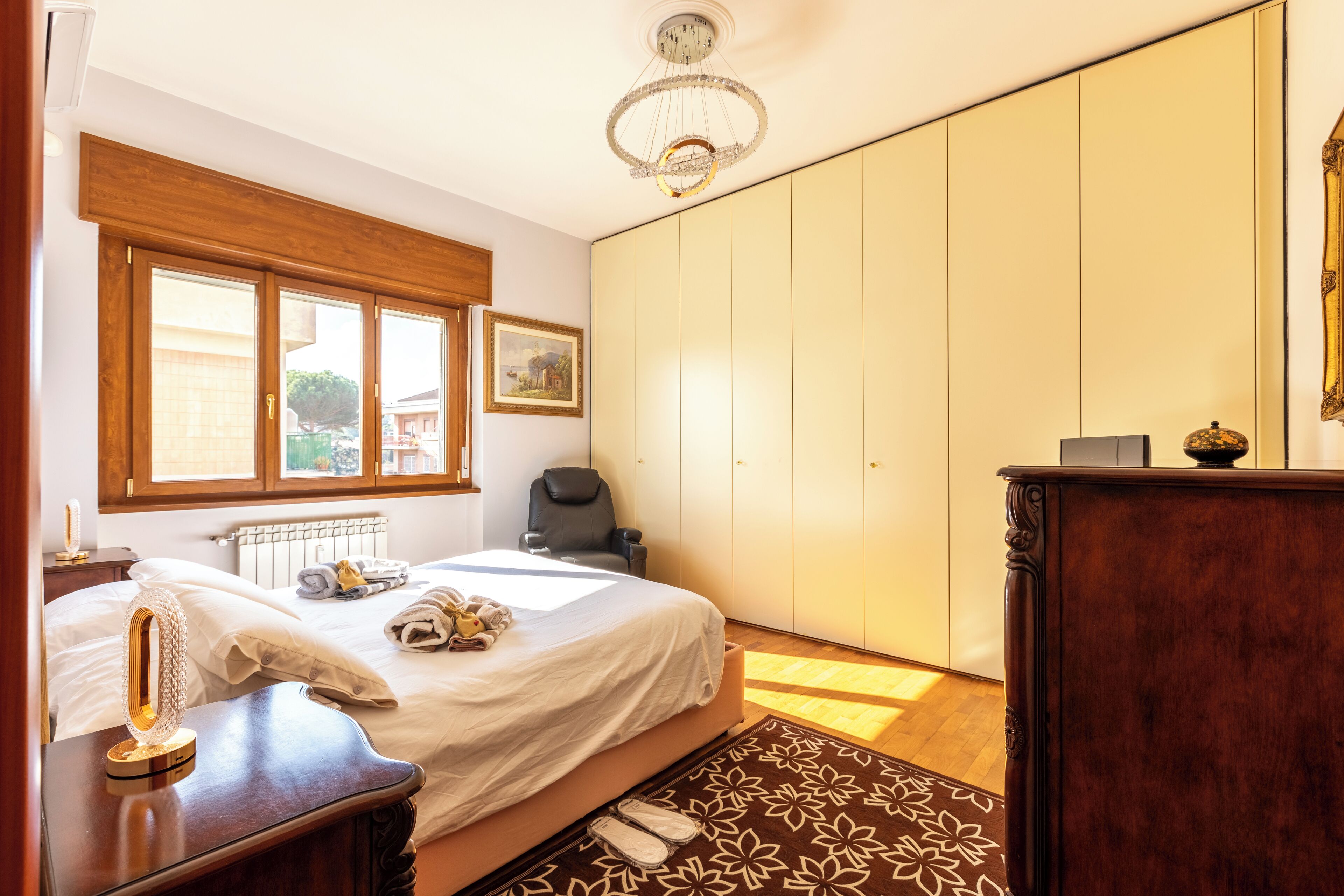 A bedroom with a bed, bedside table, dresser, and a large wardrobe.