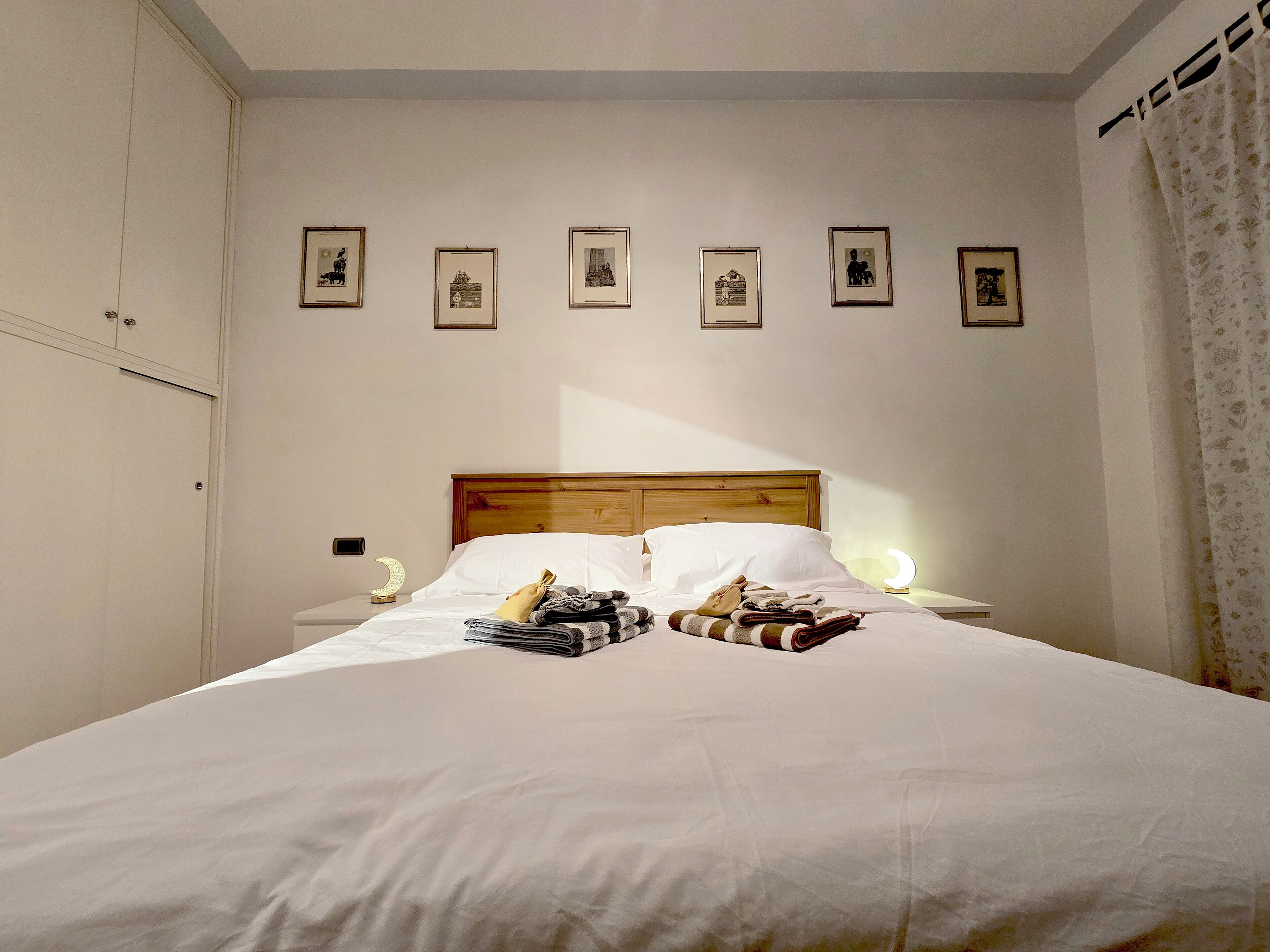 A neatly made bed with a wooden headboard, a bedside table with a lamp, and a wall with framed pictures.