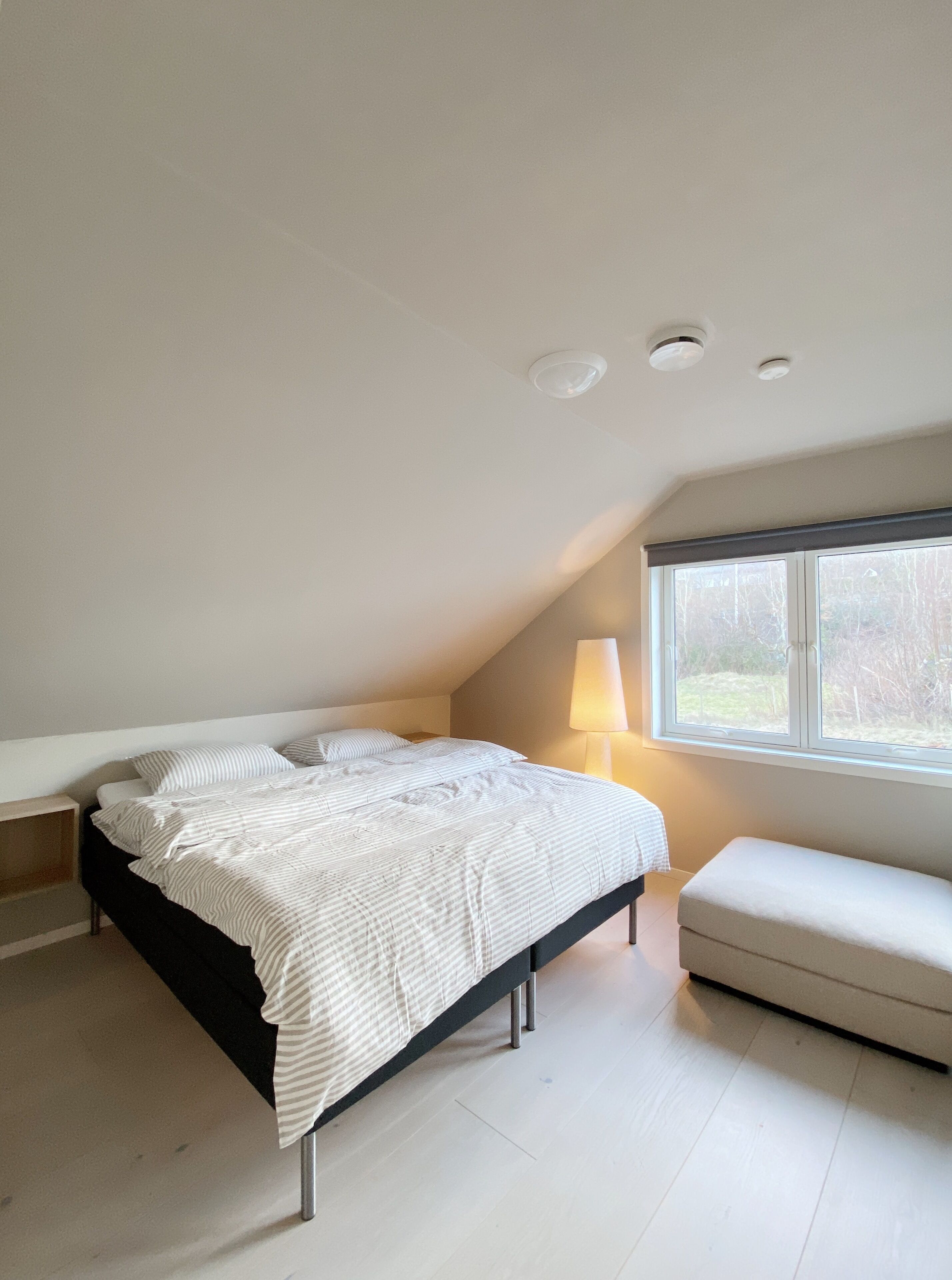 Ein Schlafzimmer mit Bett, Nachttisch, Lampe und Fenster.