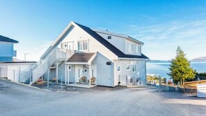 Una casa de dos plantas con un tejado inclinado y un porche con sillas, y vista al mar.