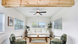 Una sala de estar con un sofá blanco, dos sillones verdes, una mesa de centro de madera y un ventilador de techo.