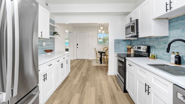 Una cocina moderna con armarios blancos, un refrigerador de acero inoxidable, un microondas y un lavaplatos.