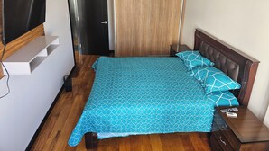 Un dormitorio con cama, televisión en un estante, armario y mesita de noche.