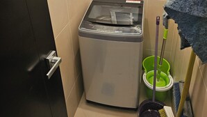 Un lavadero pequeño con lavadora, escoba y mopa.