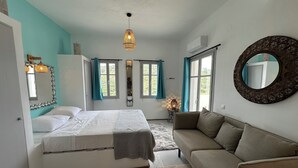 A bedroom with a bed, a sofa, a mirror, and a window with curtains.