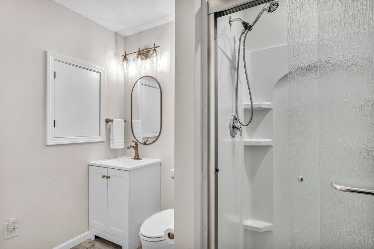 Une salle de bain comprenant des toilettes, un lavabo, un miroir et un espace douche.