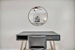 A desk with a chair, a round mirror, and a framed artwork on the wall.