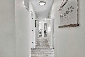 A hallway with a wooden floor, white walls, and a sign that reads 'stay awhile'.