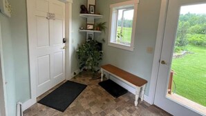 A clean, well-lit entryway with a bench, a door, a window with a view of the outdoors, and a small shelf with decorative items. - Spacious country retreat, close to Montpelier, close to nature. Smoke/pet free (Montpelier)
