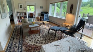 A spacious living room with a large window, a sofa, a coffee table, and a reading area with a bookshelf. - Spacious country retreat, close to Montpelier, close to nature. Smoke/pet free (Montpelier)