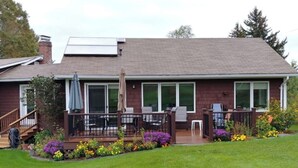 A two-story house with a covered patio, a front deck, and a small garden with flowers. - Spacious country retreat, close to Montpelier, close to nature. Smoke/pet free (Montpelier)