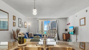 Eine moderne Küche mit einer Spüle und einem Essbereich mit einem blauen Sofa, mit Blick auf hohe Gebäude.