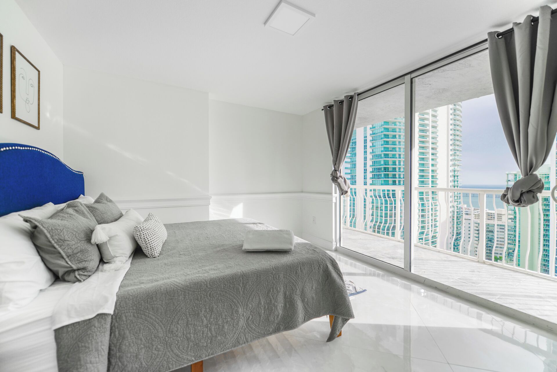 Une chambre moderne avec un grand lit, un ordinateur portable et une vue sur des immeubles de grande hauteur.