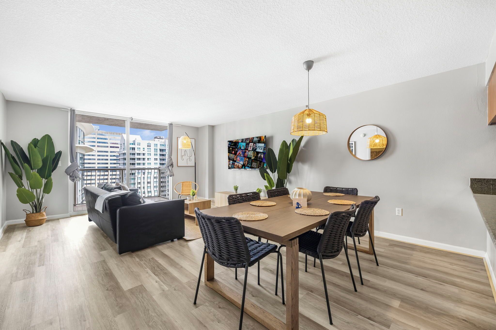 A modern apartment with a dining area, a sofa, and a large window with a city view.