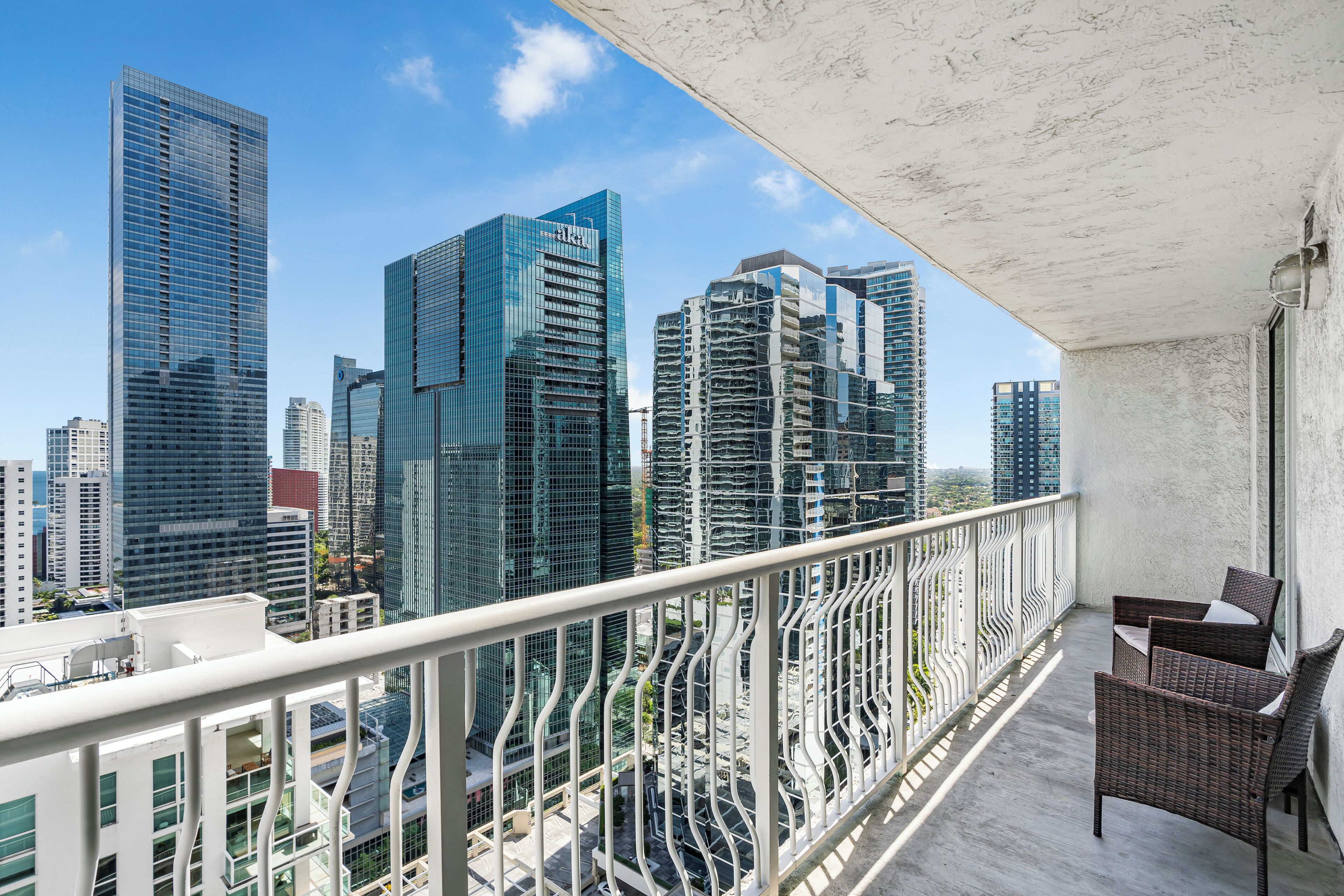 Un balcón con mobiliario de mimbre y vistas a modernos edificios altos.