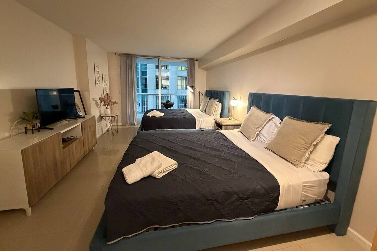 Ein Hotelzimmer mit zwei Betten, einem Fernseher, einem Schreibtisch und einem Balkon mit Blick.