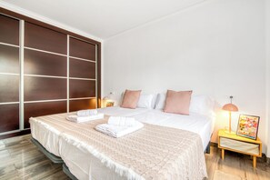 Ein Hotelzimmer mit einem großen Bett, einer Holztür, die sich schieben lässt, einem Nachttisch mit einer Lampe und einem gerahmten Bild an der Wand.