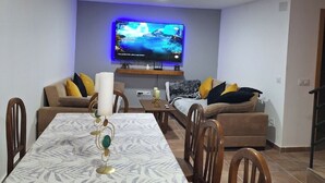 Un comedor con una mesa dispuesta para cuatro personas, un sofá y un televisor de pantalla plana montado en la pared.