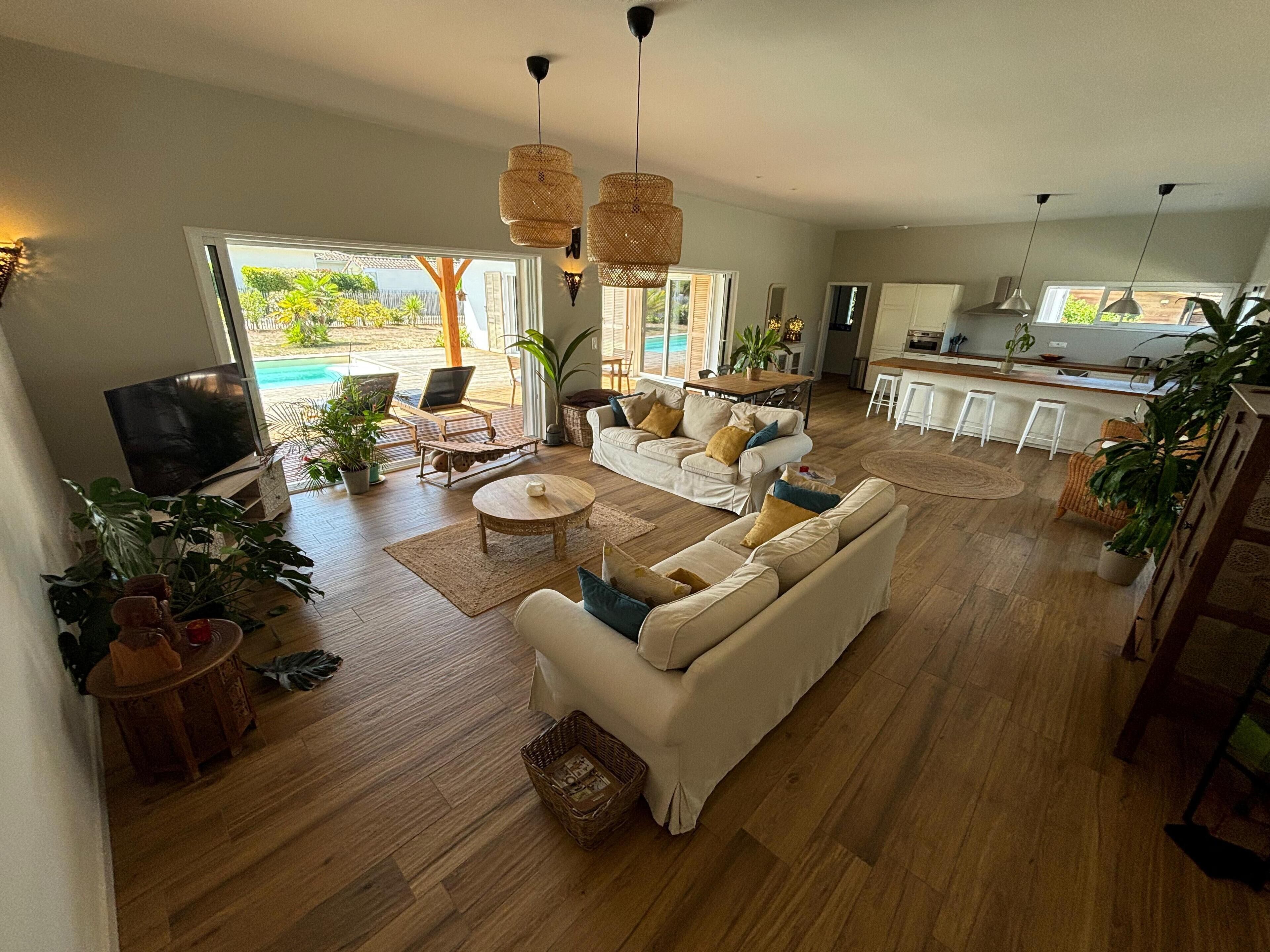 Ein geräumiges Wohnzimmer mit Sofa, Couchtisch und Fernseher, ein Essbereich mit Stühlen und eine Küche im Hintergrund.