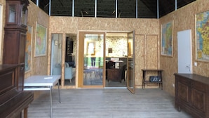 A spacious room with a high ceiling, wooden beams, a dining area, and a kitchen visible through an open door.