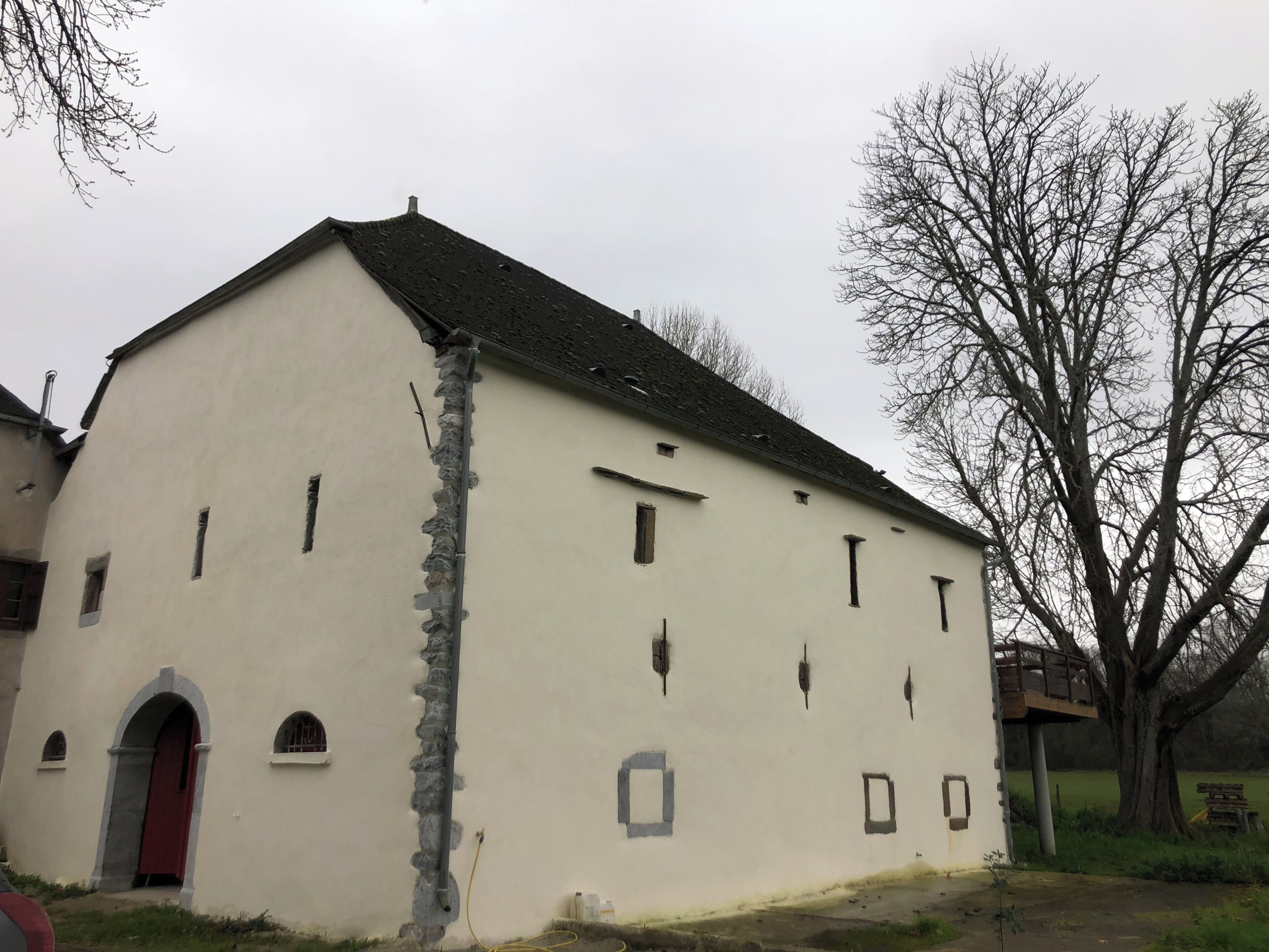 A white building with a red door, multiple windows, and a sloped roof.