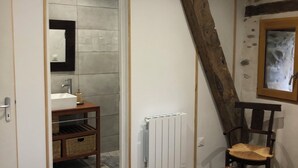 A bedroom with a wooden bed, a white radiator, a wooden chair, and a bathroom with a mirror and sink.