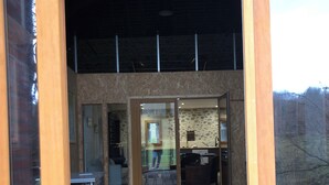 A modern building with a wooden deck, glass doors leading to an interior space, and a stone wall.