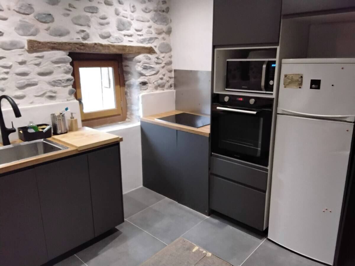 Een keuken met een stenen muur, een raam, een gootsteen, een aanrecht, een oven en een koelkast.