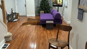 Ein modernes Wohnzimmer mit Holzboden, einem violetten Sofa, einem Holzstuhl, einem kleinen Tisch, einem Weihnachtsbaum und einem Fernseher.