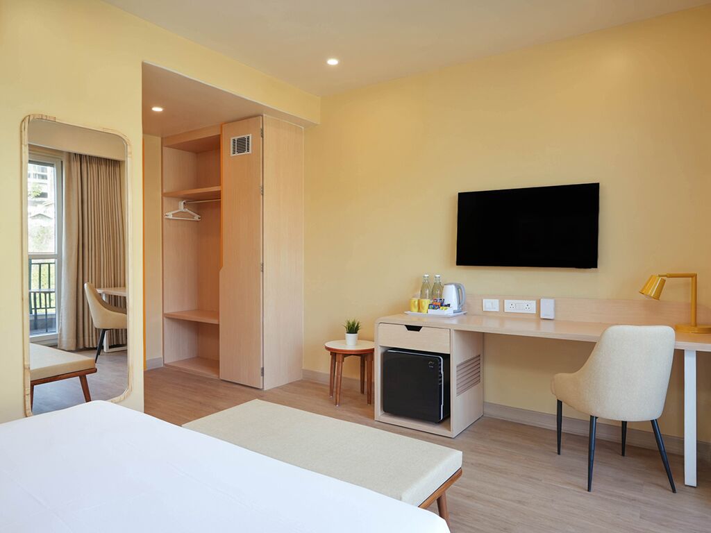 Une chambre d’hôtel comprenant un lit, un bureau avec un ordinateur, une télévision, un mini-réfrigérateur, une chaise, une petite table et un placard.