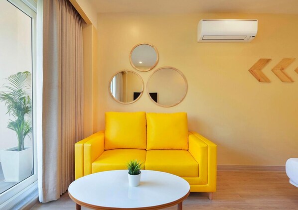 A bright yellow sofa, a round table with a potted plant, and three wall-mounted mirrors. - Bloom Boutique - Rishikesh Hills (Narendra Nagar)