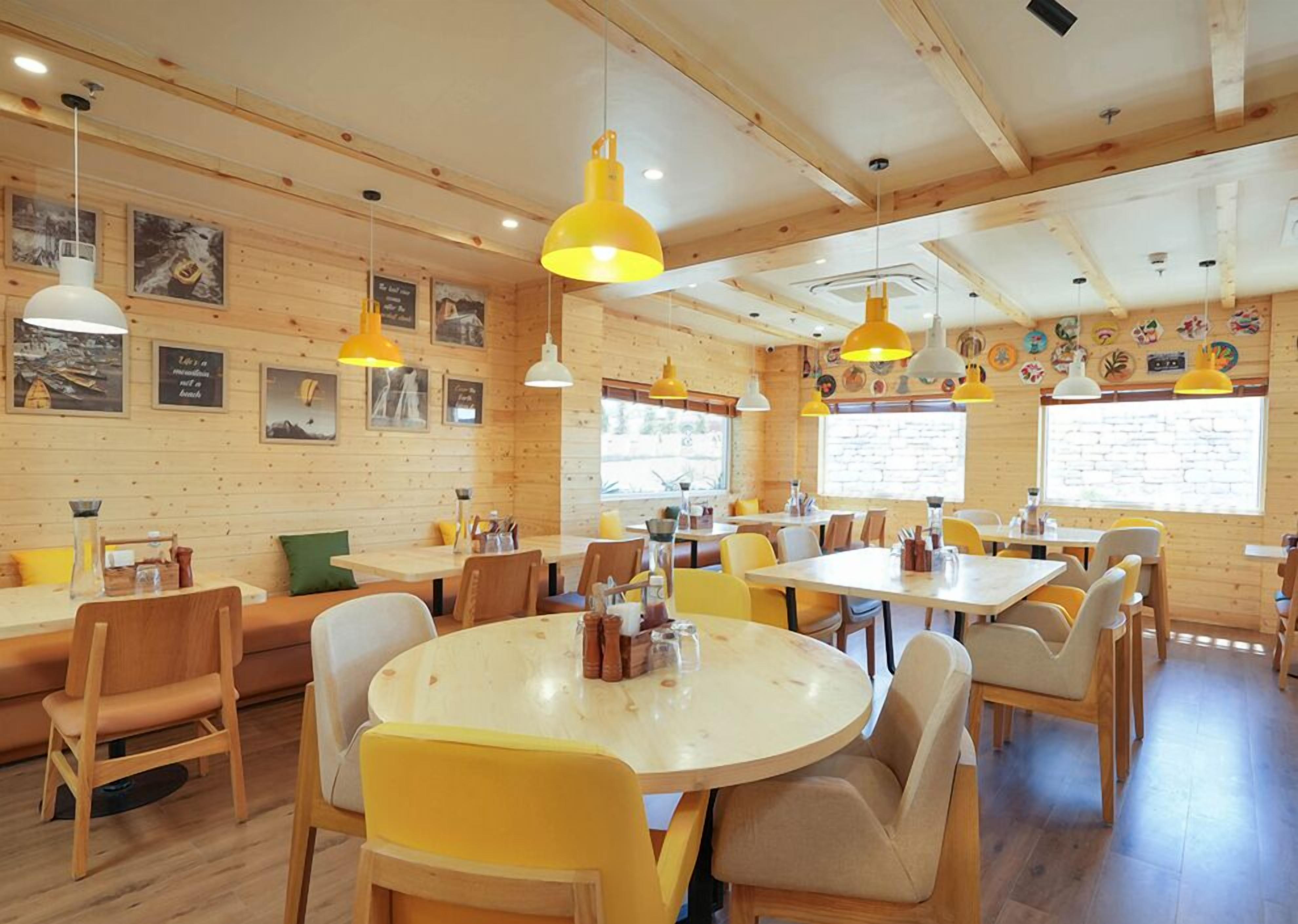 Een gezellig restaurant met houten wanden, geel en wit hangende lampen en diverse ingelijste foto's. Tafels en stoelen staan klaar voor diners.