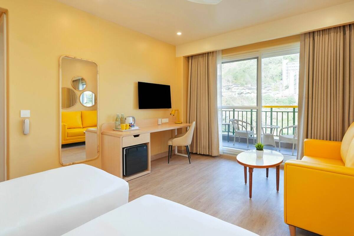 Habitación de hotel con cama, escritorio, silla, una mesita, televisor y balcón con cortinas.