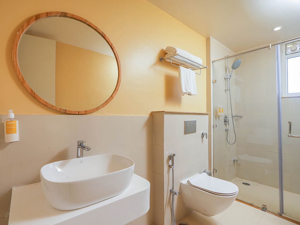 A bathroom with a large oval sink, a toilet, a glass shower enclosure, and a round mirror on the wall.