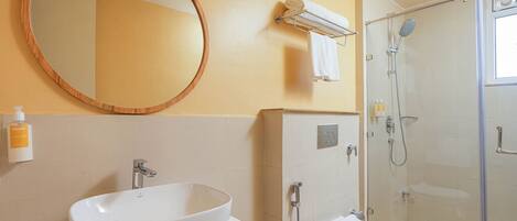 A bathroom with a large oval sink, a toilet, a glass shower enclosure, and a round mirror on the wall.