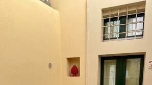 Ein kleiner Sitzbereich im Freien mit Tisch und Stühlen, eine Tür mit Fenster und eine kleine, rote Dekoration an der Wand.