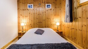 Un dormitorio con paneles de madera, una cama, dos lámparas de noche y dos cuadros en la pared.