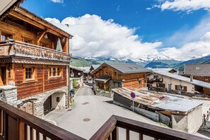 A traditional wooden building with balconies, a stone archway, and a clear view of snow-capped mountains in the background. - Chalet sleeps 20 Skis-on, Historic Village of Montchavin (LA PLAGNE) (La Plagne-Tarentaise)