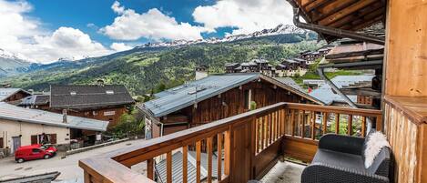 A wooden balcony overlooking a mountain village with traditional buildings and a snowy backdrop.