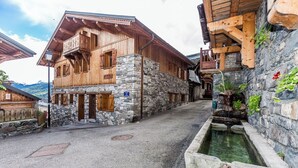 Un edificio tradicional de madera con paredes de piedra, un balcón y una pequeña fuente.