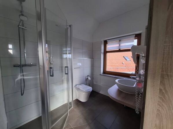 A modern bathroom with a glass shower enclosure, a toilet, and a sink with a vanity. - Hotel Bike & Hike (Wildeck)