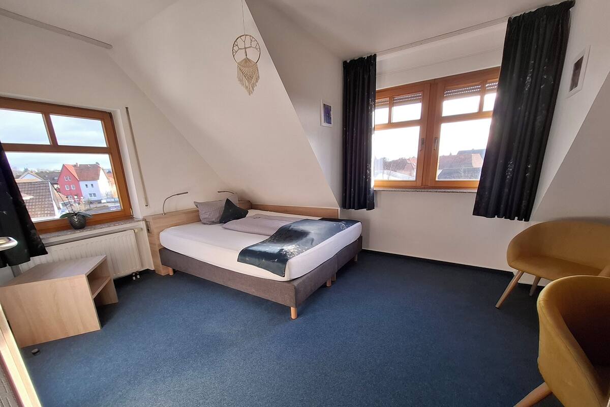 A room with a bed, a desk, a chair, a radiator, and a window with curtains.