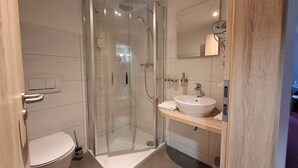 A modern bathroom with a glass-enclosed shower, a white sink, and a mirror above it. - Hotel Bike & Hike (Wildeck)