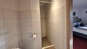 A modern bathroom with white tiles, a shower area, and a visible toilet. - Hotel Bike & Hike (Wildeck)