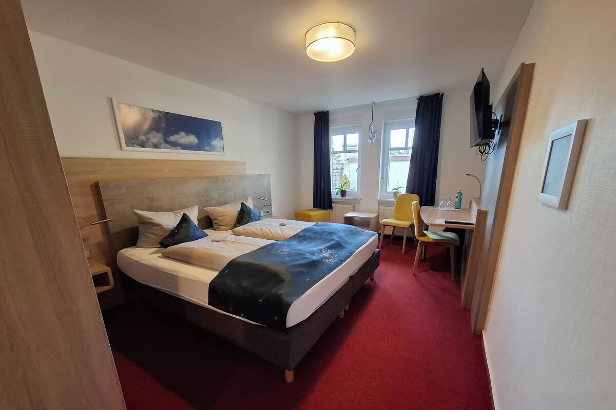 A hotel room with a double bed, a desk, a chair, and a window with curtains.