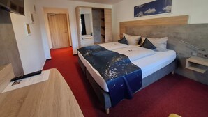 A hotel room with a large bed, a desk, a chair, a nightstand, and a mirror. - Hotel Bike & Hike (Wildeck)